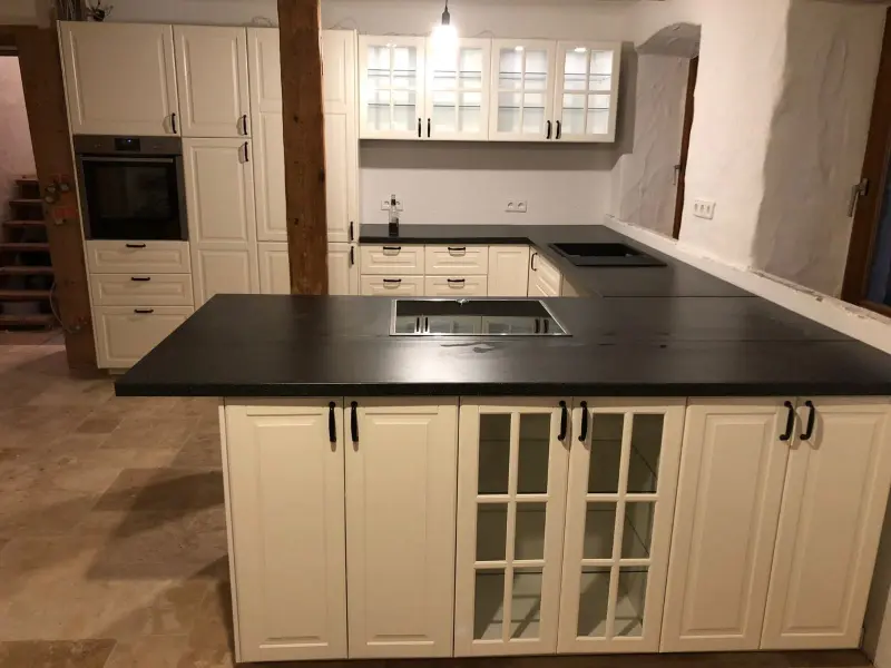 Prostrana bijela kuhinja s otokom, tamnom radnom pločom i staklenim vitrinama - montaža kuhinja Hrvatska